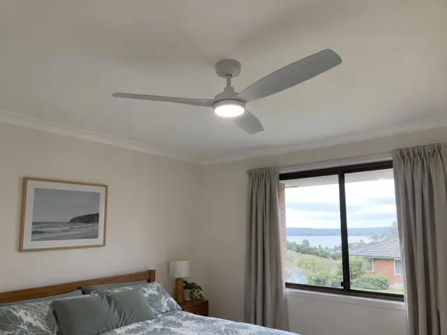 Bedroom with a modern ceiling fan and lit light over a bed, beside a window and curtains in Empire Bay