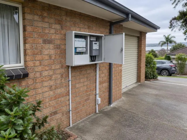External electrical switchboard and meter box on a brick house wall beside a garage in Saratoga